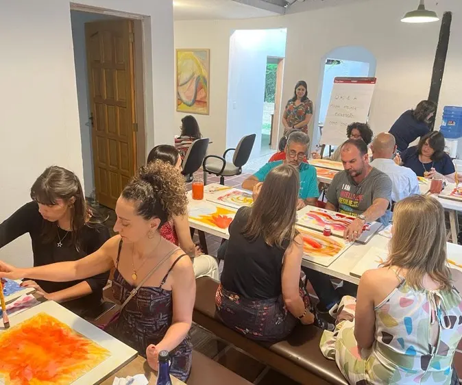 Integrantes pintando em aquarela ao redor de uma mesa