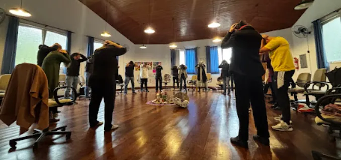 Integrantes em pé formando um círculo em sala ampla