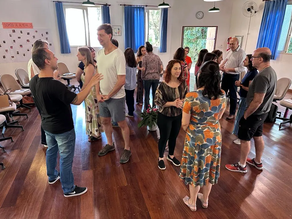 Integrantes em pé conversando em duplas e trios na sala ampla